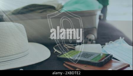 Image of digital padlock and shield over smartphone with qr code, luggage, hat and mask on bed Stock Photo