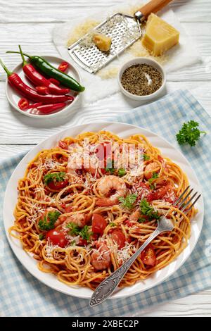 shrimp fra diavolo with spaghetti, tomato based hot sauce sprinkled with grated parmesan cheese on white plate on white wooden table with fork, vertic Stock Photo