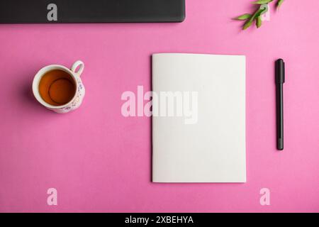 Top view of a book mockup on an office desk table with laptop, pen, cup, and leaves on a pink background Stock Photo