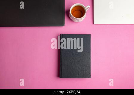 Top view of a book mockup on an office desk table with laptop, cup, and notepad on a pink background Stock Photo