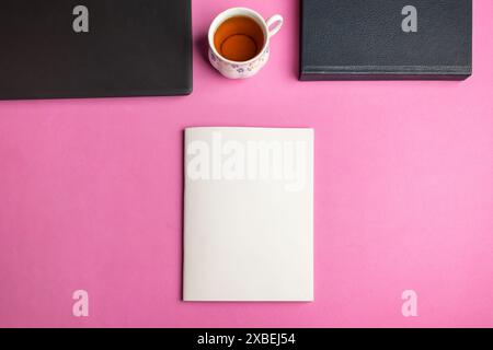 Top view of a book mockup on an office desk table with laptop, cup, and notepad on a pink background Stock Photo