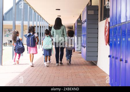 A biracial teacher walking with students in school hallway with blue lockers Stock Photo