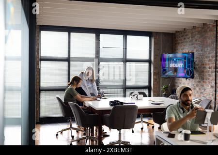 Asian businesswoman discussing project with young Caucasian woman in modern office. Large windows and exposed brick walls create open, collaborative w Stock Photo