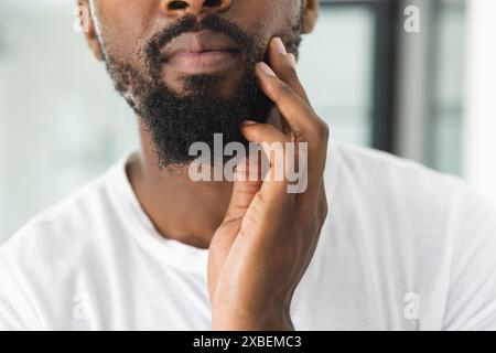 African American young man touching his beard thoughtfully, at home Stock Photo