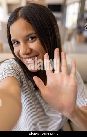 Biracial young woman smiling and waving at camera, at home Stock Photo