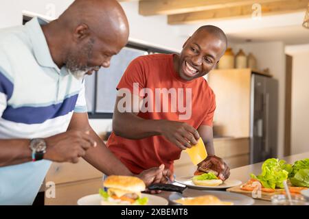 African American father and son preparing burgers together in modern kitchen. Bright natural light fills room, highlighting the warm and inviting atmo Stock Photo