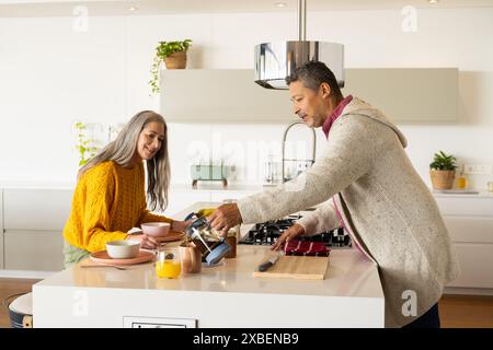 A biracial mature couple prepares breakfast in a modern kitchen, at home. The bright and airy space features white cabinets, stainless steel appliance Stock Photo