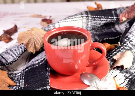 There is a cup of tea on the table, and around it there are dry leaves and a warm scarf. Stock Photo