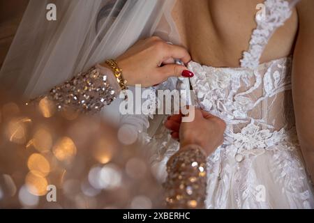 A close-up of a bride's dress being buttoned up by a bridesmaid with sequined sleeves. Stock Photo
