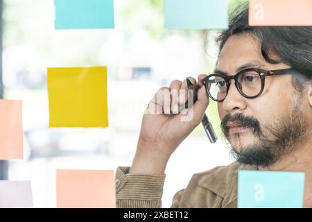 A young businessman is writing down ideas on sticky notes on the wall Stock Photo