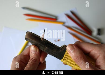 Photo of process of sharpening pencils with a clerical knife. Human hands. Metal knife. On the background are white papers and colored pencils. Creati Stock Photo