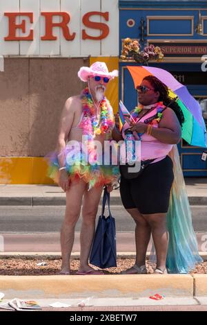 An interesting Couple, one  in a cowboy hat, rainbow-colored tulle tutu and leis in conversation at Pride Parade 2024, Albuquerque, New Mexico, USA. Stock Photo