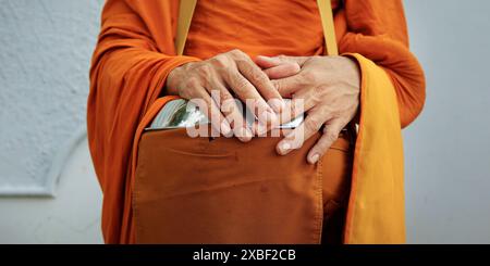 hand of monk dressing orange robe, holding bowl during reception of alms Stock Photo