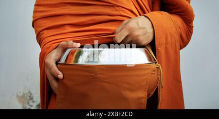 hand of monk dressing orange robe, holding bowl during reception of alms Stock Photo