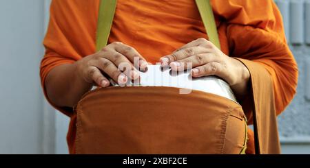 hand of monk dressing orange robe, holding bowl during reception of alms Stock Photo