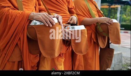 hand of monk dressing orange robe, holding bowl during reception of alms Stock Photo