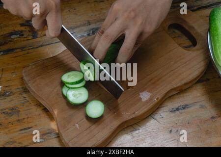 green cucumbers are cut with a knife in the kitchen. close-up green cucumbers in the kitchen hands close-up cut into slices Stock Photo