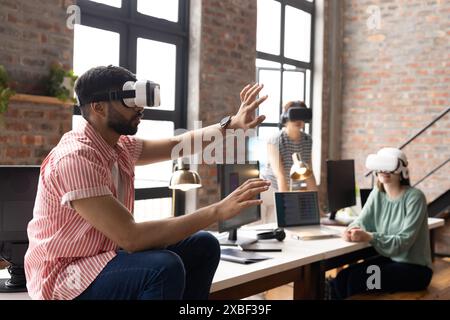 Diverse colleagues in office using vr headset. working on laptop in a modern office with large windows, creating innovative atmosphere, unaltered Stock Photo