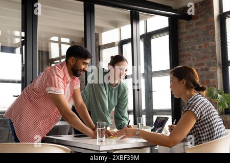 Diverse team collaborates; young woman and colleague share ideas. Modern office with large windows and natural light, creating bright workspace, unalt Stock Photo