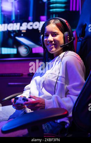 Biracial young woman wearing headset playing video games, smiling at camera, at home Stock Photo