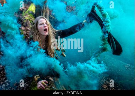 A woman throws blue smoke in a forest. Shallow depth of feld Stock Photo