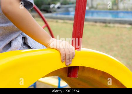 kids toddler playing at the playground, holding onto the yellow slide Stock Photo