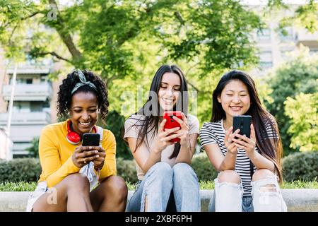 Three multiracial women using mobile phone outdoors. Stock Photo
