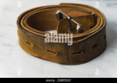 old and worn out brown leather belt on top of white table Stock Photo