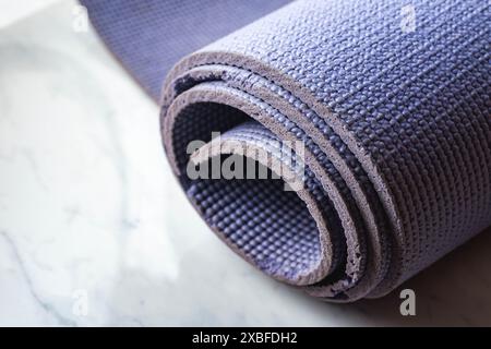 A yoga mat is rolled up on a marble countertop. The mat is purple and has a slightly worn appearance Stock Photo