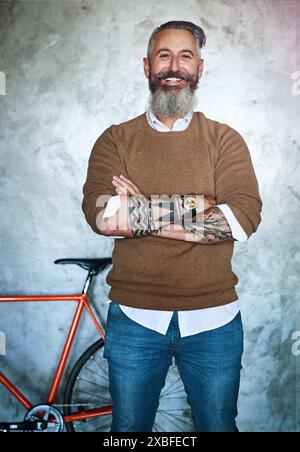 Businessman, portrait and happy with arms crossed or tattoos in creative office with bicycle and confidence. Mature professional, employee and smile Stock Photo