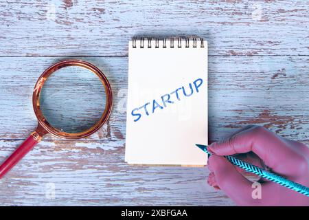 Startup word concept handwritten inscription in a glove with a pencil and a magnifying glass lying next to it on the boards Stock Photo