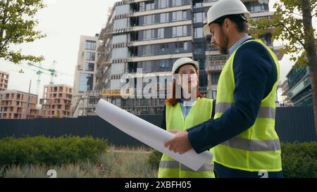 Two architects urban build workers Caucasian colleagues partners in safety hat and reflective vest talking discuss city blueprint builders engineers Stock Photo