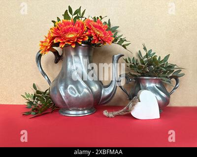 Vintage Metal Teapots with Bright Red Flowers and Greenery on Red Tablecloth Stock Photo