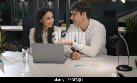 Cheerful Caucasian talking smiling laughing with laptop computer pc in office colleagues male manager and female businesswoman at desk working Stock Photo