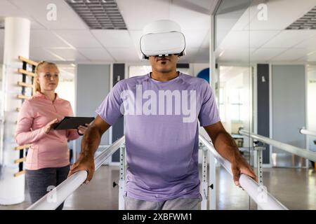A biracial man wearing VR headset using parallel bars for rehabilitation Stock Photo