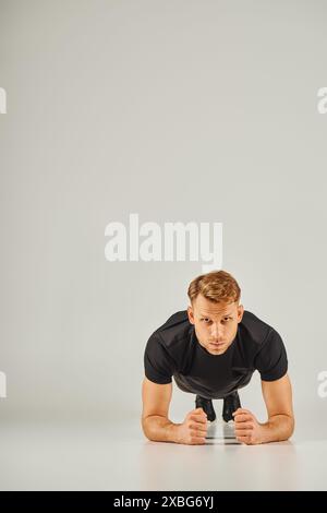 A young athletic man in active wear, performing push ups on a grey background in a studio. Stock Photo