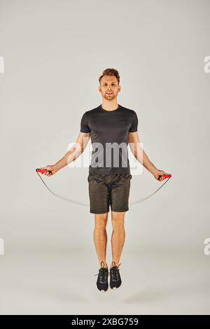 A young sportsman in active wear is energetically jumping with a skipping rope in front of a white background. Stock Photo