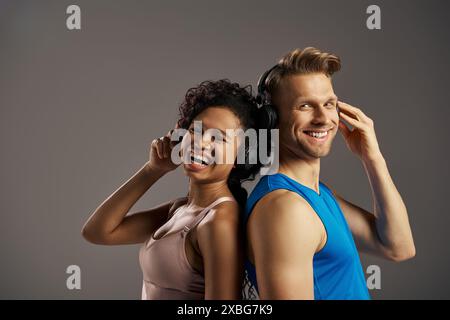 A young man and woman in activewear are immersed in music, listening through headphones with expressions of joy and connection. Stock Photo