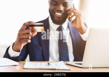Happy young man holding credit card, talking on phone Stock Photo