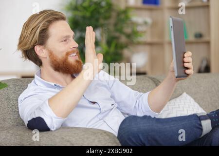 smiling man using tablet for vidn©o chat on his couch Stock Photo