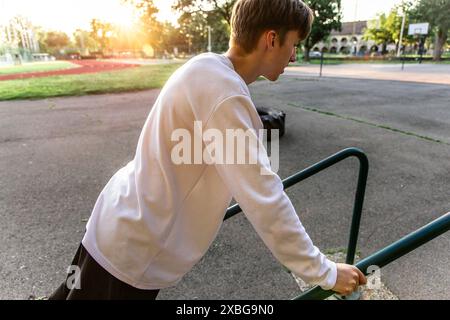 Young Man Doing Dips on a Park Railing at Sunset Stock Photo
