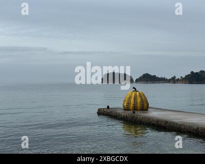 The famous Yayoi Kusama Yellow Pumpkin in Naoshima Island on a cloudy day with the island and the sea in the background. Stock Photo