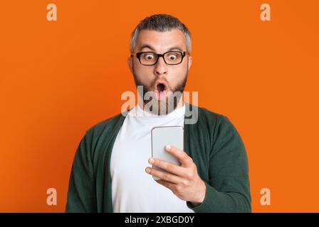 Man With Beard Expressing Shock While Looking At Smartphone Stock Photo