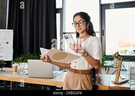 Young indian woman wearing glasses, holding a folder, and checking her phone. Stock Photo