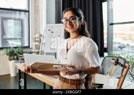 A professional indian woman with glasses holding a folder in an office setting. Stock Photo