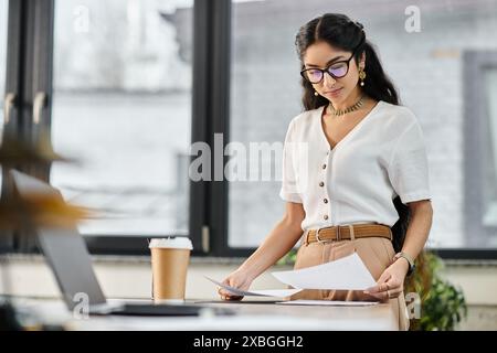 A indian woman in glasses stands at a desk with papers. Stock Photo