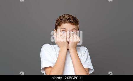Fearful teen boy biting nails on grey background Stock Photo