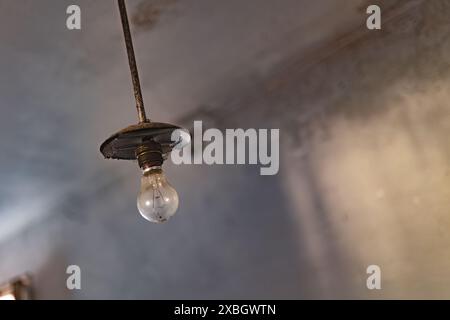 Close-up of a single light bulb in an old, rusty ceiling fixture, showcasing the wear and tear of time. Stock Photo