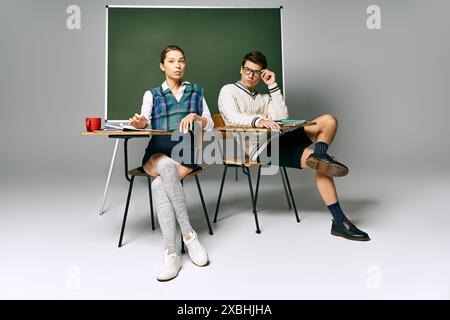Young man and woman discussing ideas while seated at a desk in front of a green board. Stock Photo