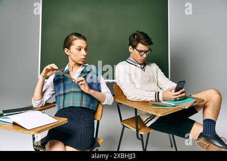 Elegant man and woman sitting in front of green chalkboard, engaged in learning. Stock Photo
